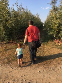 Dad walking with daughter through apple orchard